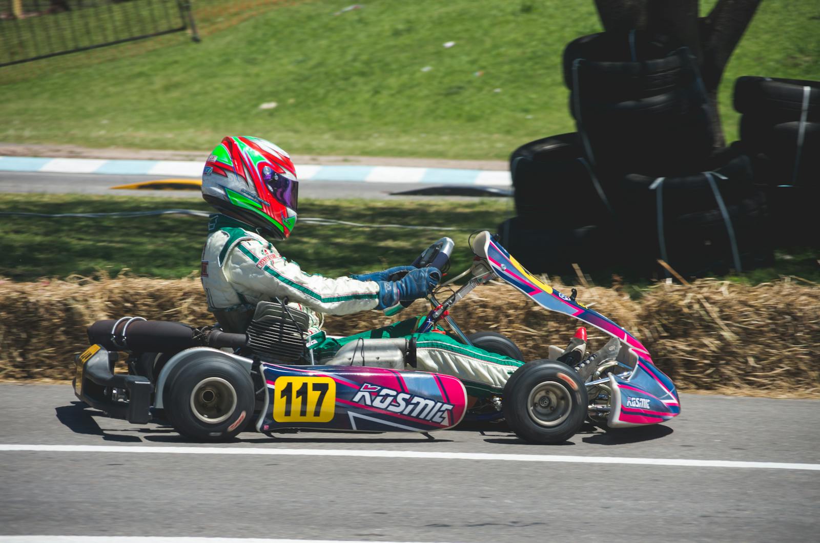 Go-kart racer speeding on an outdoor track under a sunny day with safety gear.